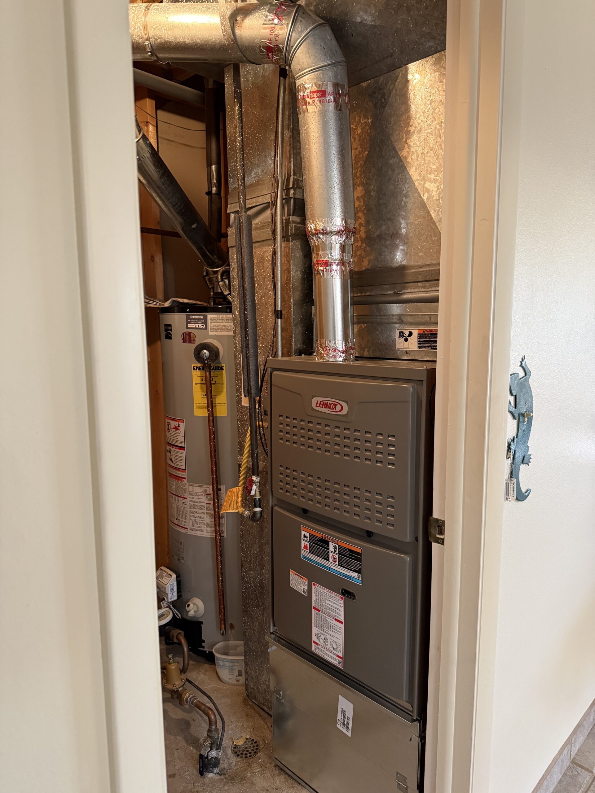 A home utility closet containing a water heater and a Lennox furnace with visible ductwork and pipes.